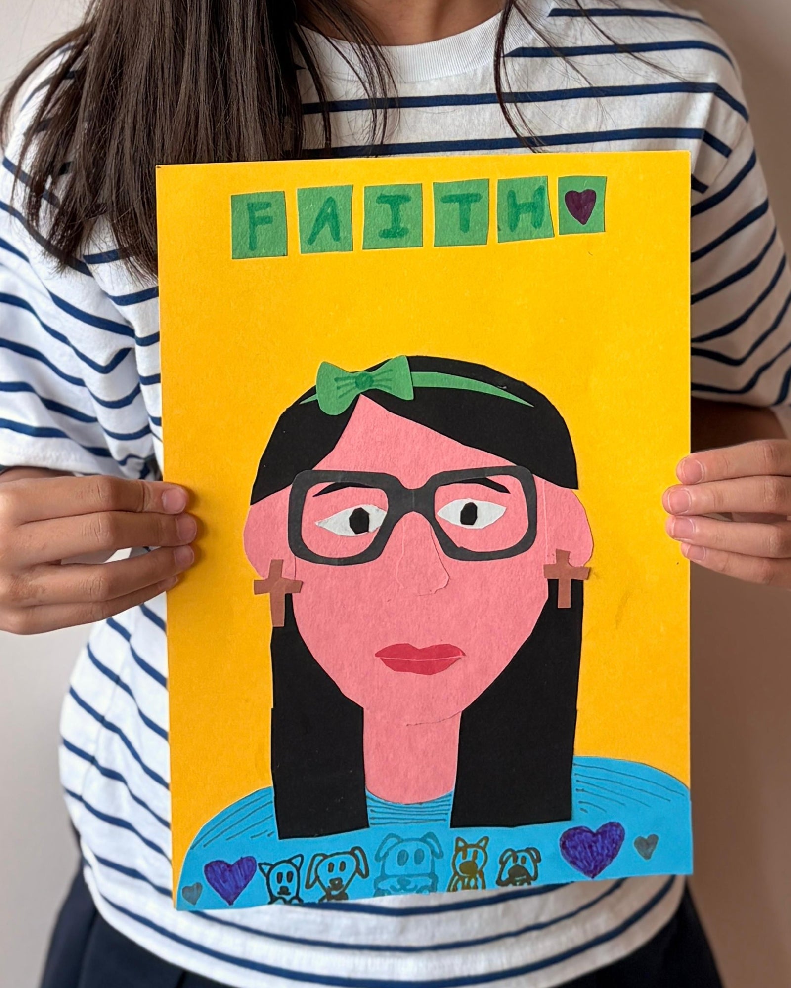 Young girl holding a drawing of herself with glasses against a plain background